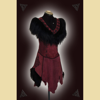 Dress made of burgundy suede. Decorated with lavish sheepskin trim, black trimmings, and black ornaments at the neckline and side panels. The skirt section shows the natural edges of the goat suede.
